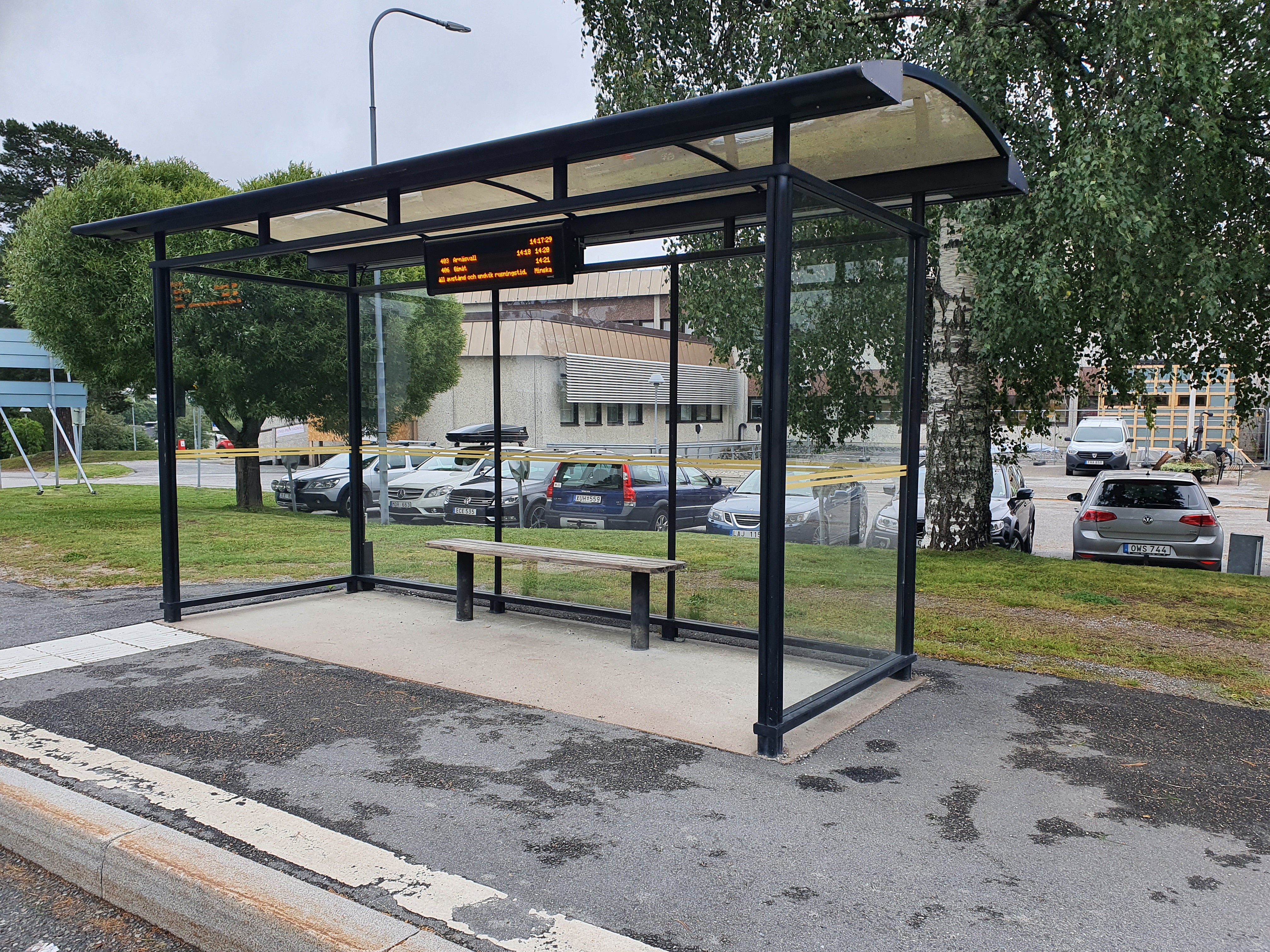 En busskur i glas och metall. en parkering med bilar bakom