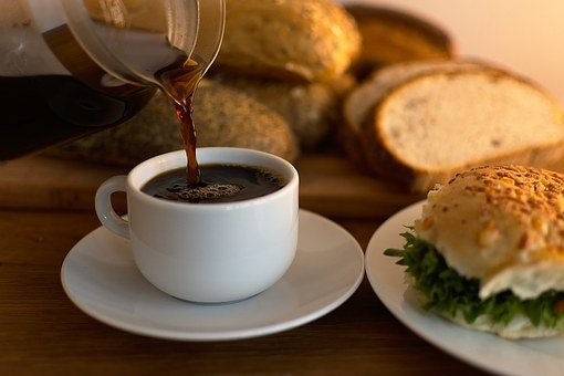 Smörgåsar på en assiett, uppskuret bröd bredvid. Någon får kaffe upphällt i kopp.