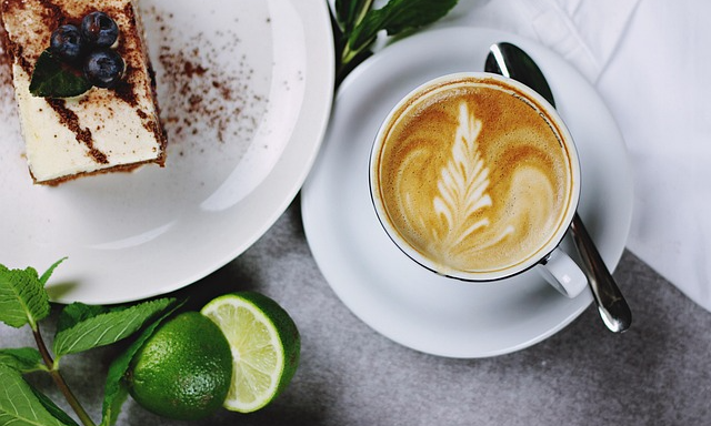 Bakelse till vänster med blåbär på. En kopp kaffe med mönster till höger. En delad lime i förgrunden.