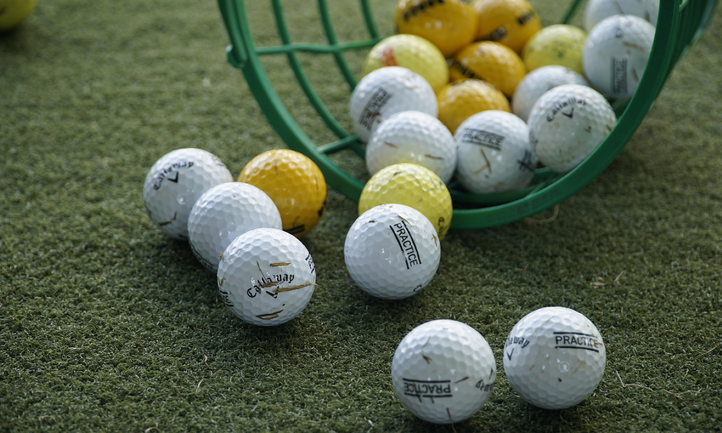 Golfbollar i olika färger i en liggande grön korg på golfbana.