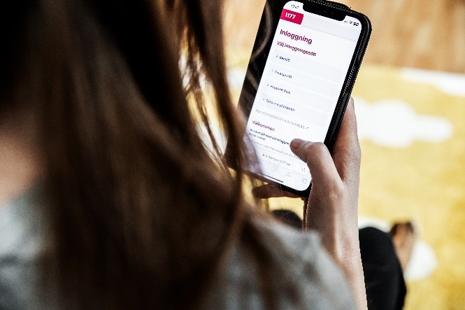 Appen 1177 i mobilfönstret. En person loggar in. Endast personens fingrar och lite av håret som syns.