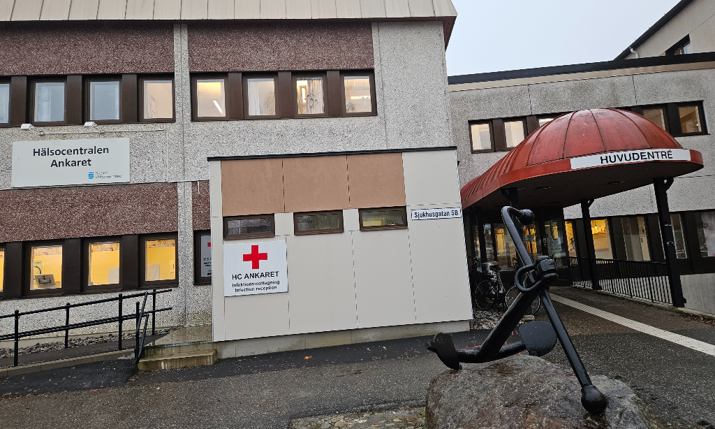 Hälsocentralen Ankarets entré med rappad ljus fasad. Ett stort svart järnankare på en sten framför entrén.