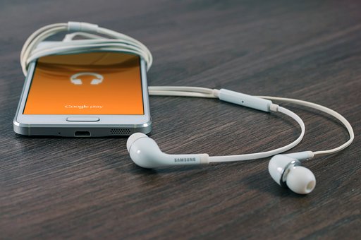 Mobiltelefon och trådlösa hörlurar på ett brunt bord. Mobiltelefonens skärm är orange