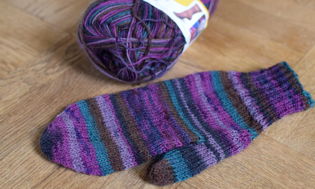 En stickad vante med nystan i olika lila toner.