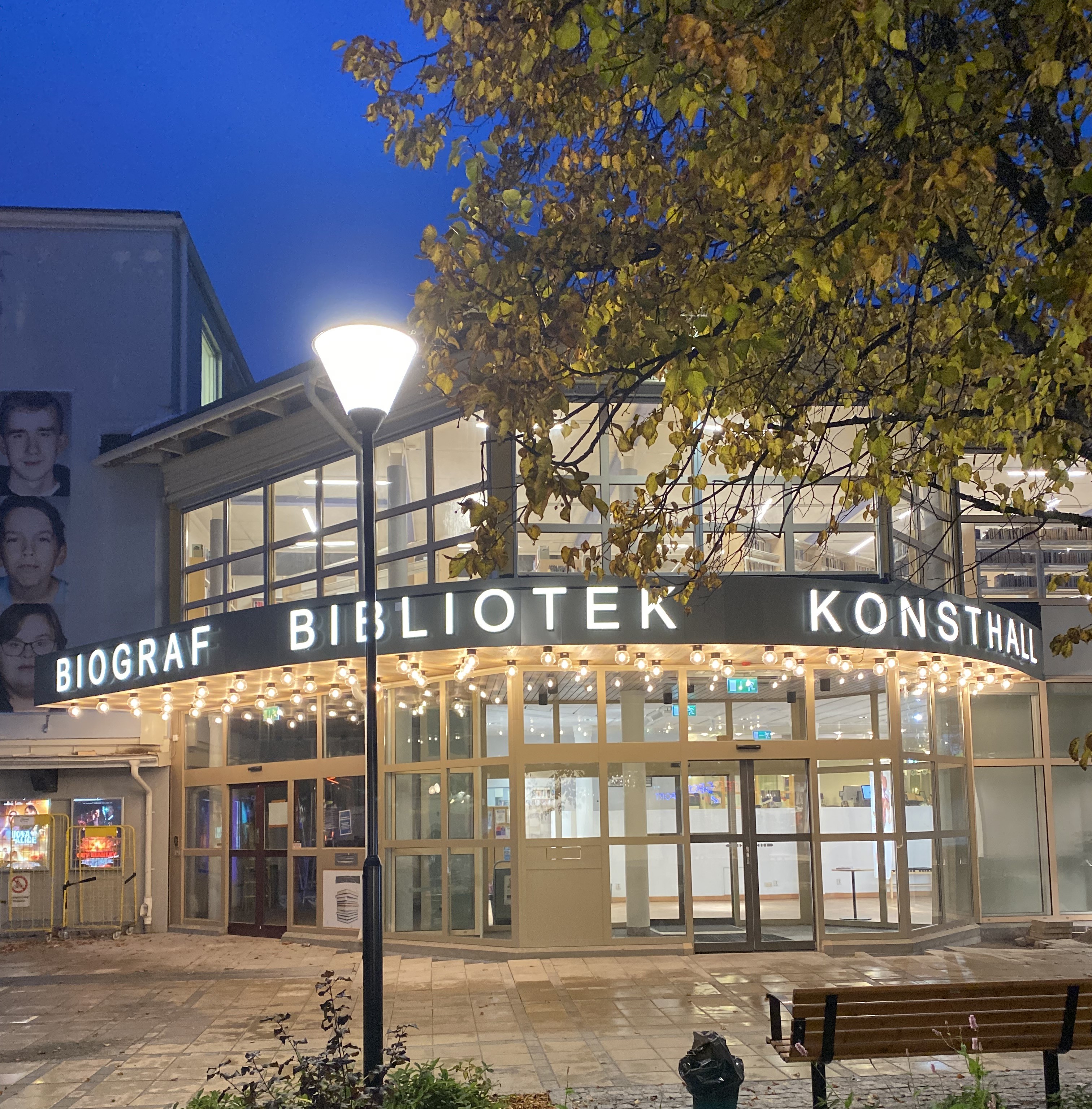 Nya upplysta entrén i Kramfors. Kvällsbild och det står Biograf Bibliotek Konsthall med stora tydliga bokstäver ovanför entrén.