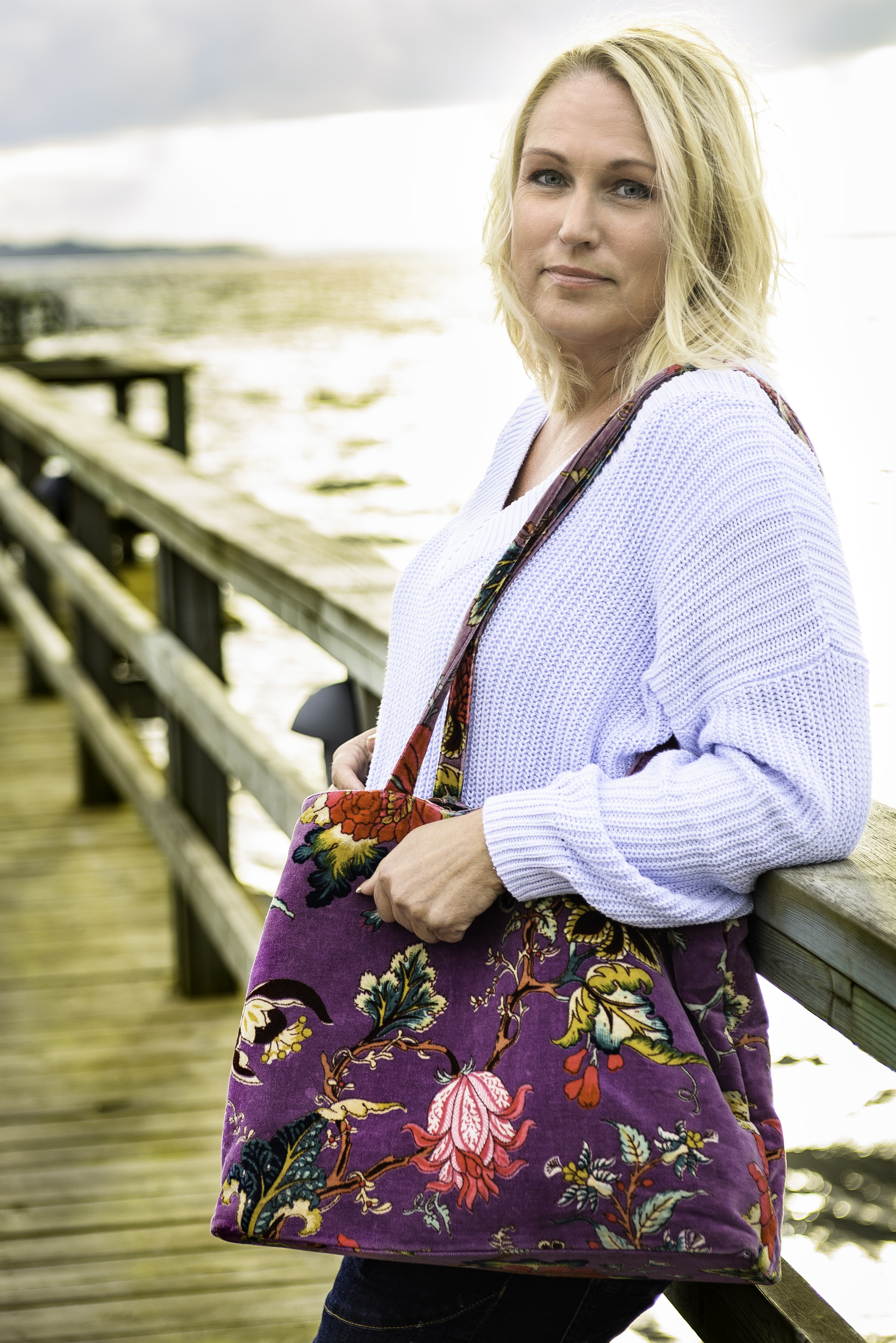 Ann Gomér står vid ett räcke. Hon har en färgglad väska hängande överöver axeln.