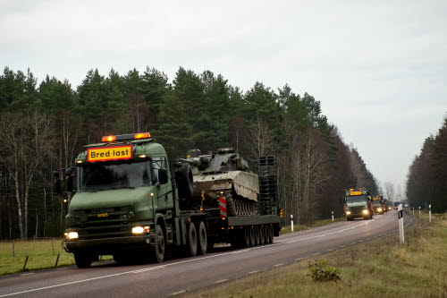 Lastbilar med militära transporter på väg. Skog på var sida av vägen.