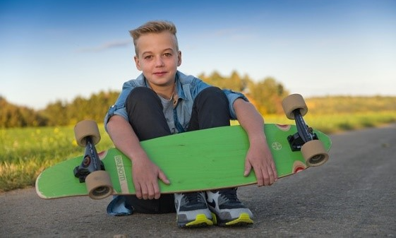 Pojke sitter vid vägkanten. Han håller i en skateboard med grön undersida..