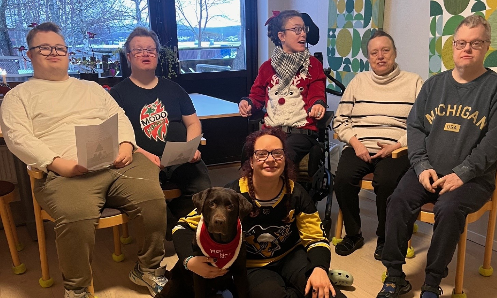 Hunden Penny ligger på golvet framför en grupp på daglig verksamhet.